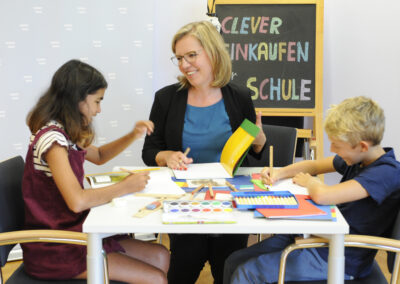 Foto zum Schuleinkauf 2020, Zwei Kinder sitzen zusammen mit Leonore Gewessler am Tisch und malen